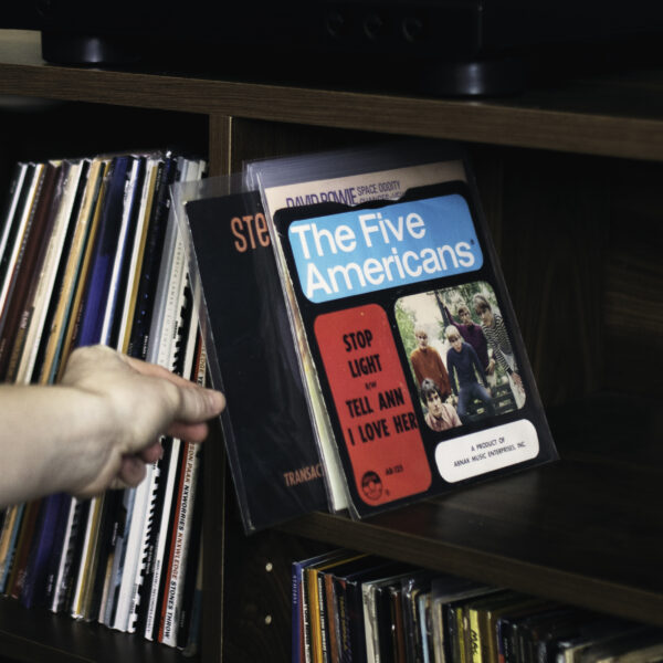 Hand pulling a 45 RPM picture sleeve protected by a clear polyethylene outer sleeve from a record shelf